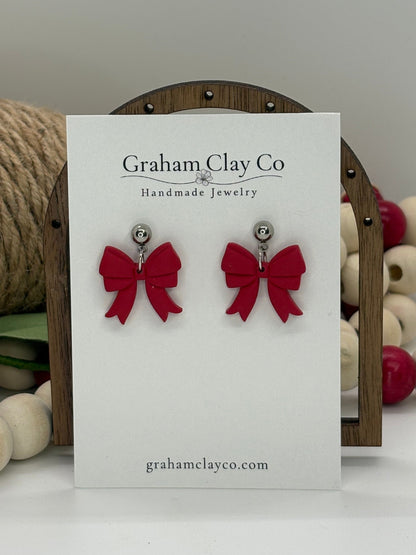 Red bow earrings on a card with 'Graham Clay Co' branding, displayed against a neutral background.