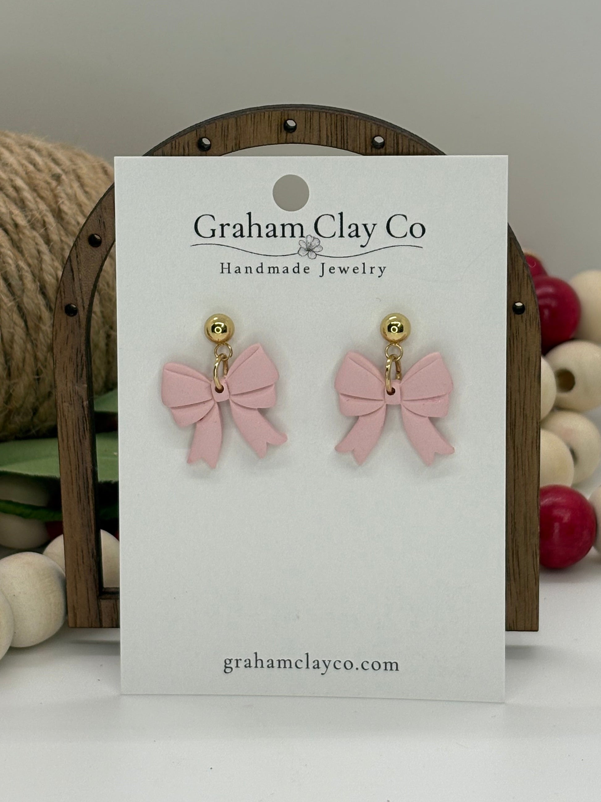 Pink bow earrings on a branded card with decorative background